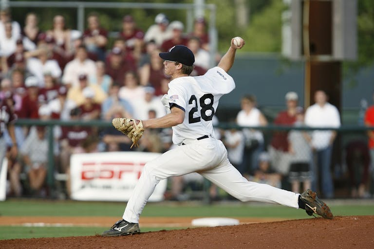 A baseball player in uniform pitches during a game with a crowd of spectators.