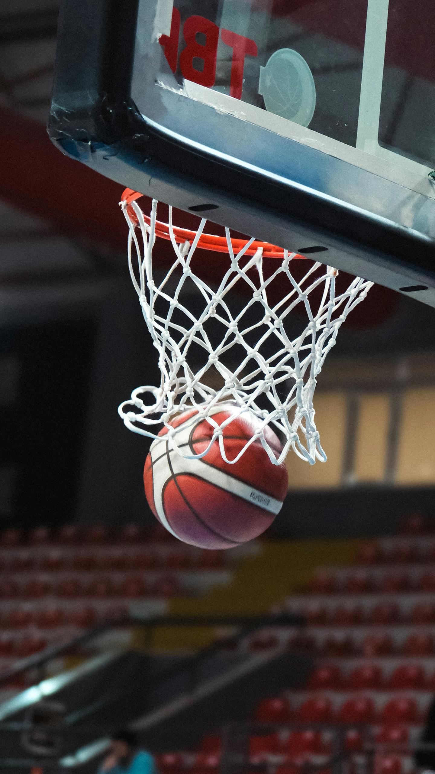 A basketball going through a hoop in an indoor sports arena captured mid-action.