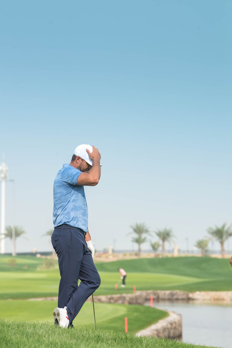 A golfer in a blue shirt stands disappointed on a sunny golf course, contemplating a missed shot.