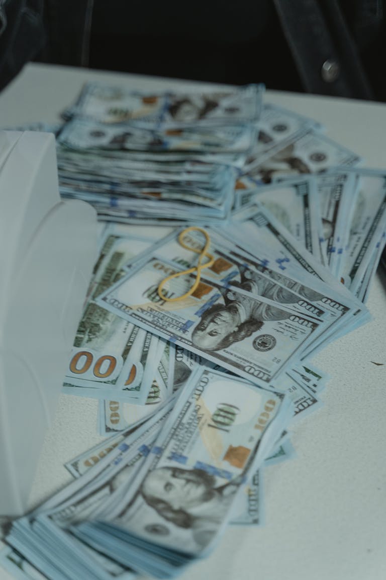 A pile of US dollar bills neatly stacked and secured with a rubber band on a white surface.