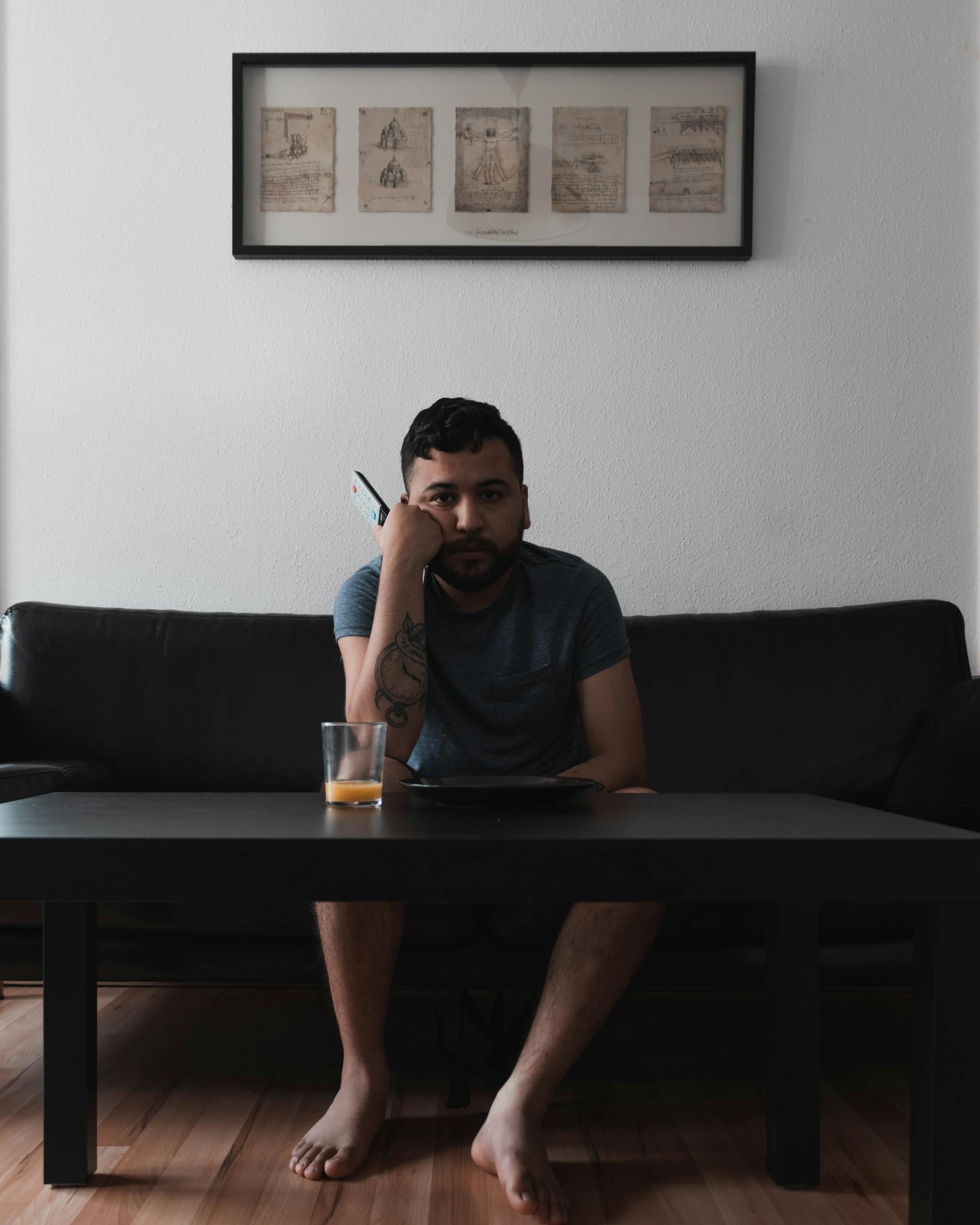 An adult man sitting on a sofa indoors holding a remote, juice on table.