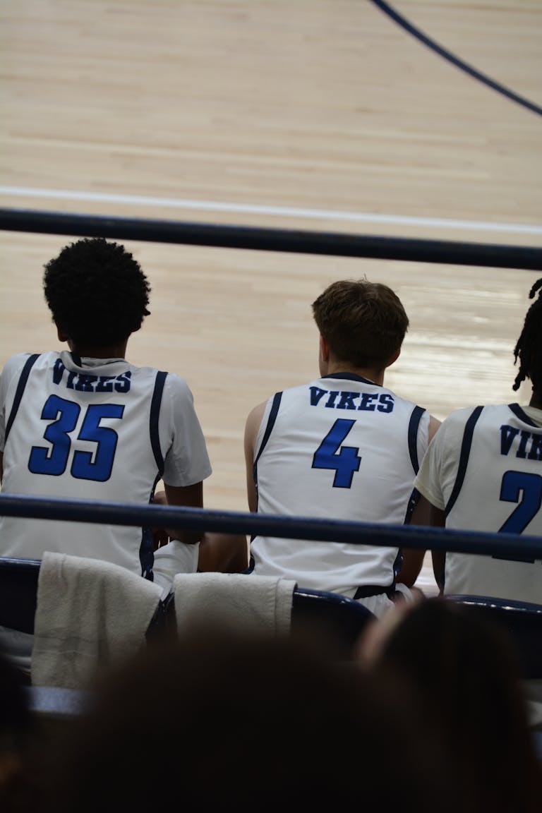 Basketball players sitting on the bench during a game, wearing team jerseys.
