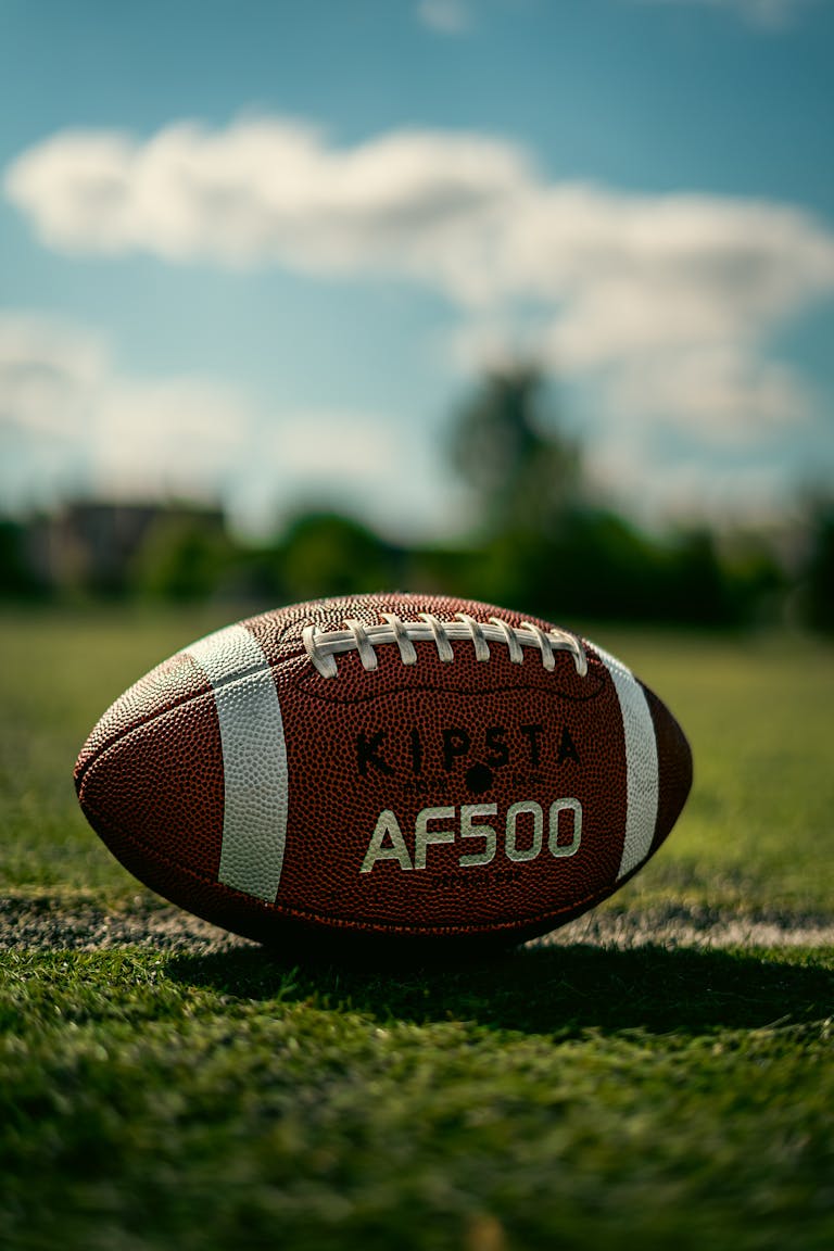 Detailed photo of a Kipsta AF500 football resting on a grassy field under a blue sky.