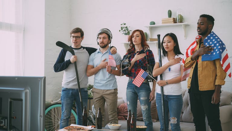 Diverse group of friends watching sports on TV, shown with American flags indoors.