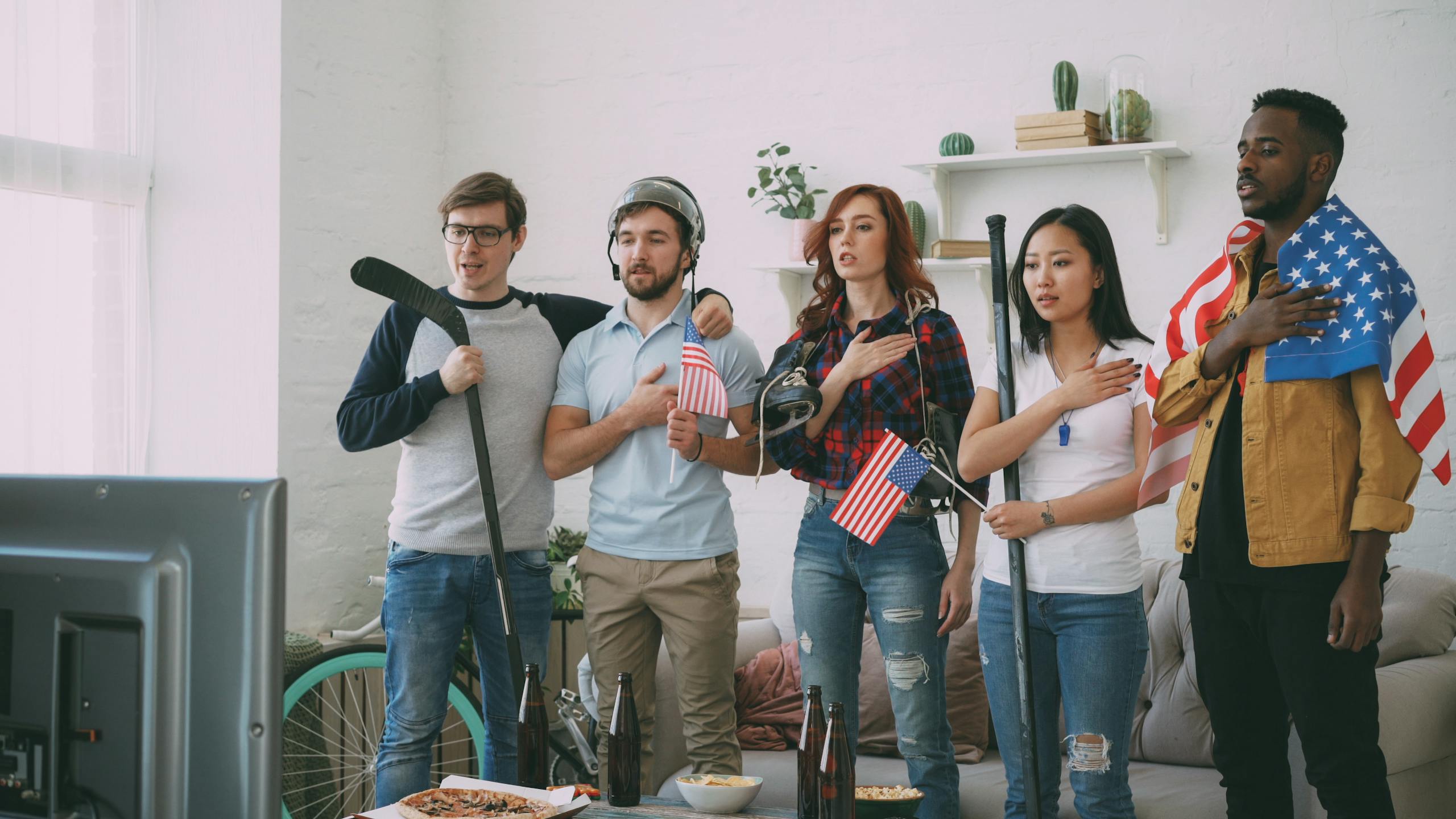 Diverse group of friends watching sports on TV, shown with American flags indoors.