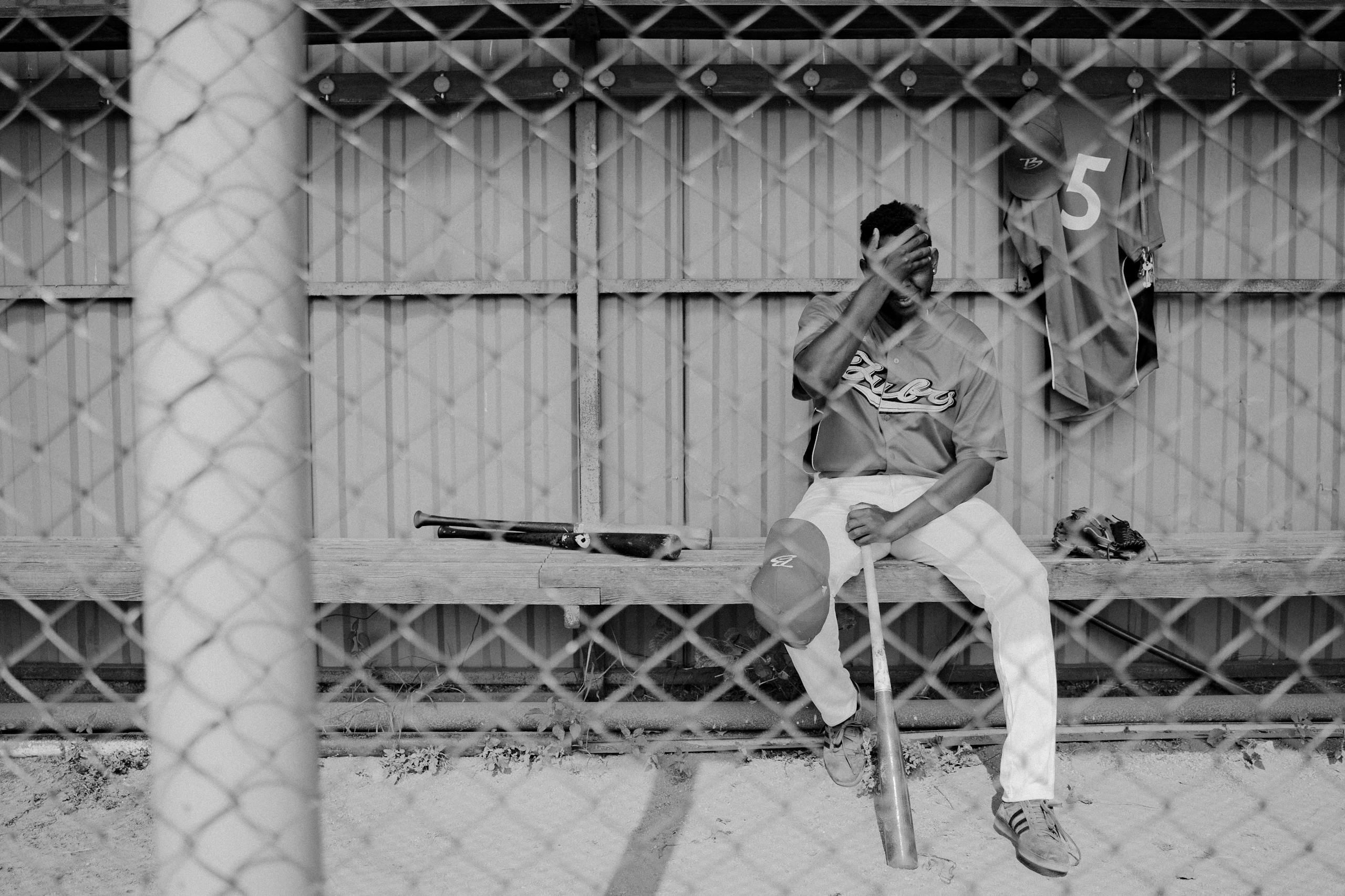 Emotional black and white photo of a baseball player sitting on a dugout bench, looking dejected.