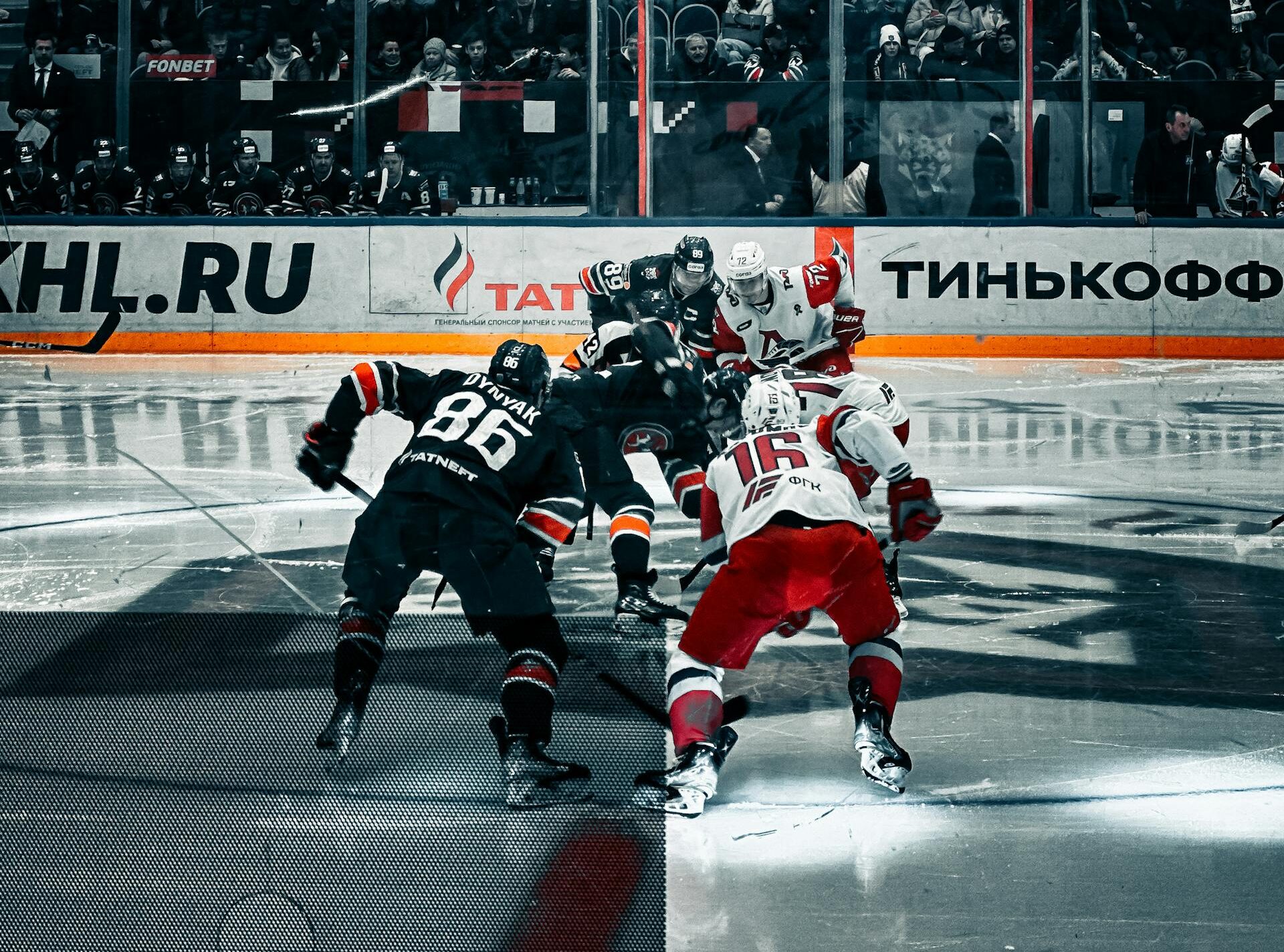 Players face off during a professional ice hockey match in an arena with the audience watching.