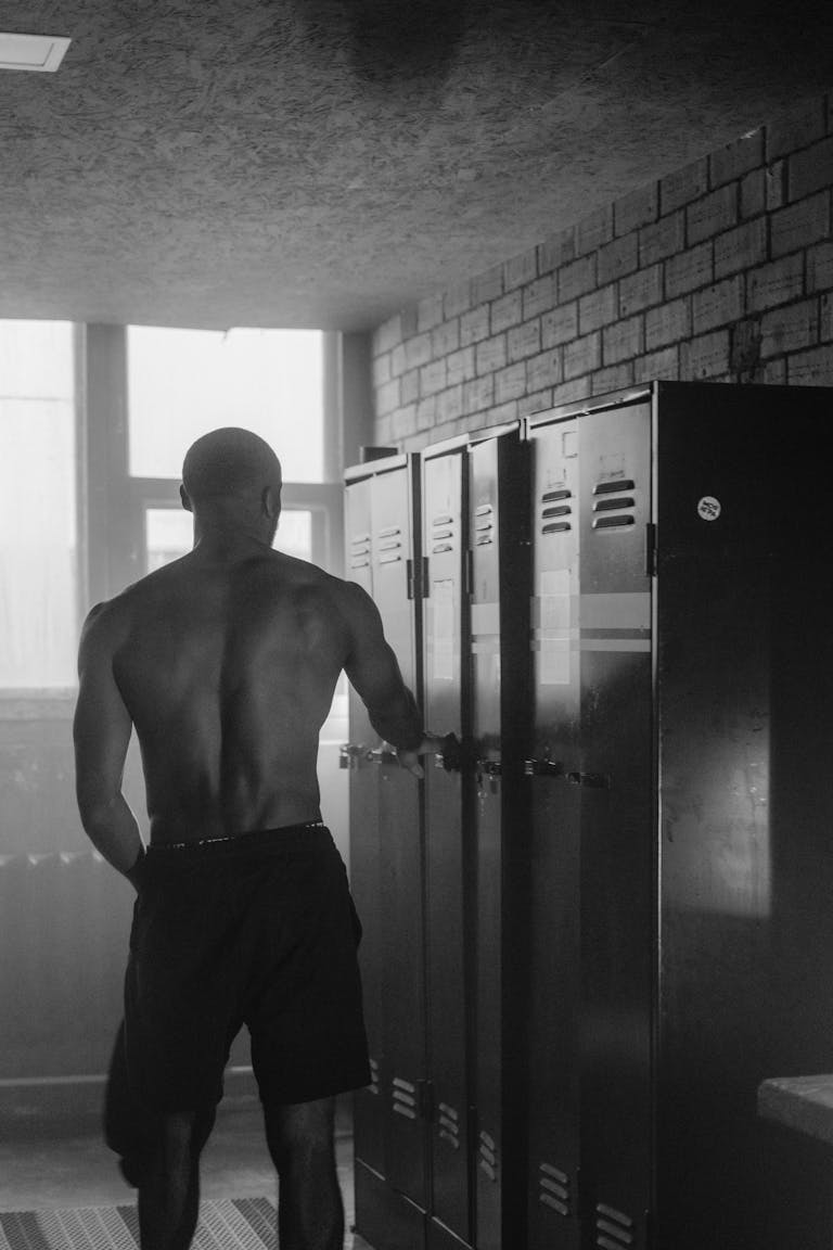 Shirtless man standing in a locker room, getting ready for a workout.