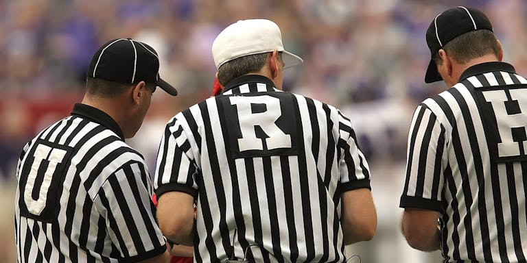 Three referees in black and white striped uniforms at a sports event.