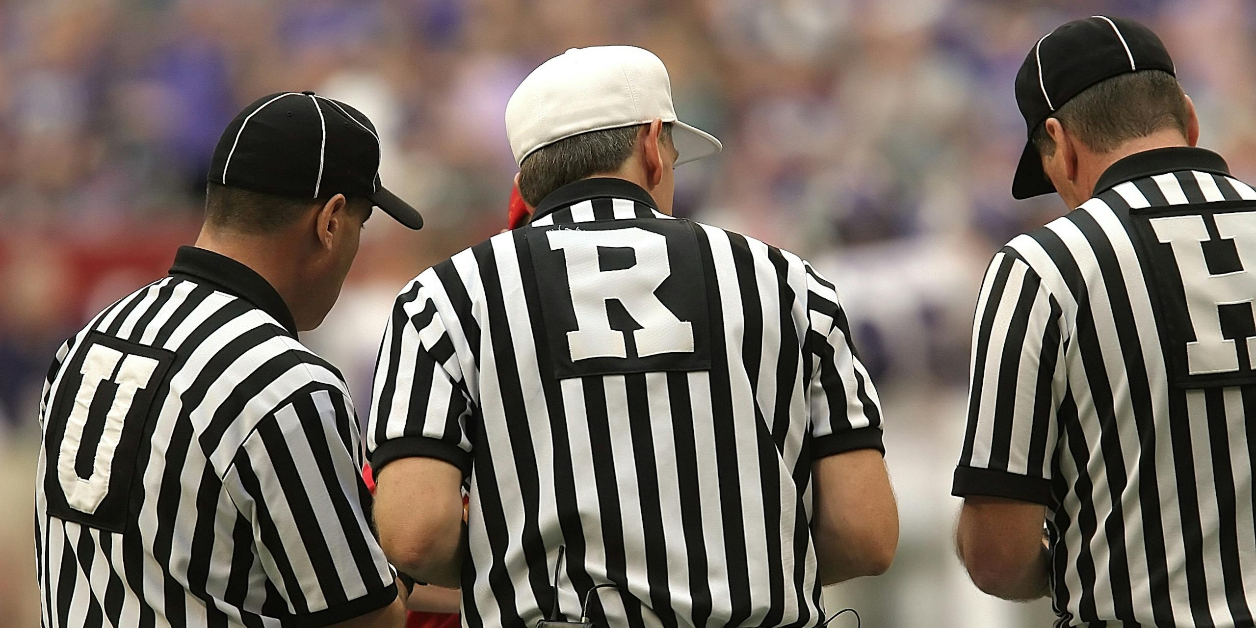 Three referees in black and white striped uniforms at a sports event.