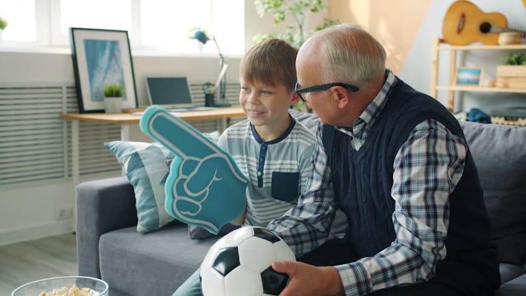 A grandfather and grandson bonding over soccer with foam finger indoors.