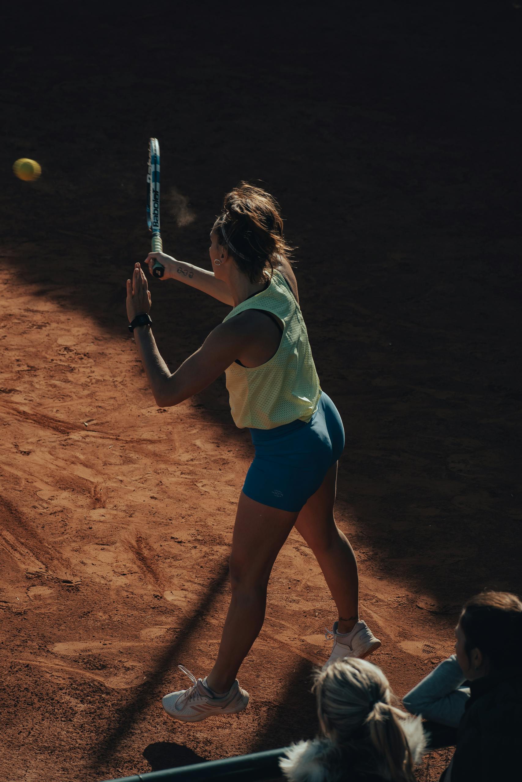 A woman hitting a tennis ball with a racket during a match on a clay court, showcasing athletic skill.