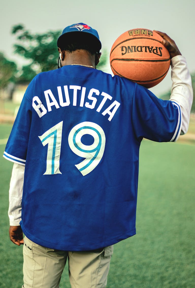 Back view of a person in a blue jersey holding a basketball on a field.