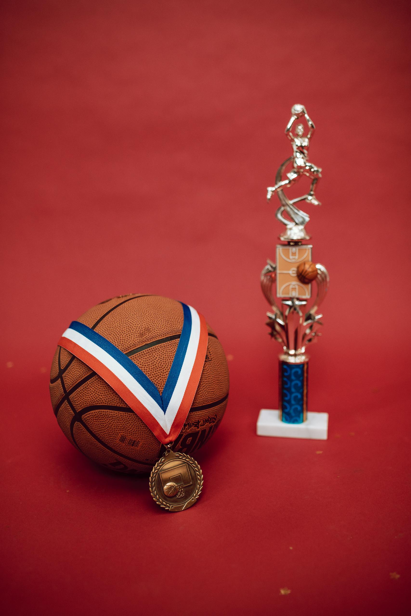 Basketball with gold medal and trophy on a red background representing achievement and victory.