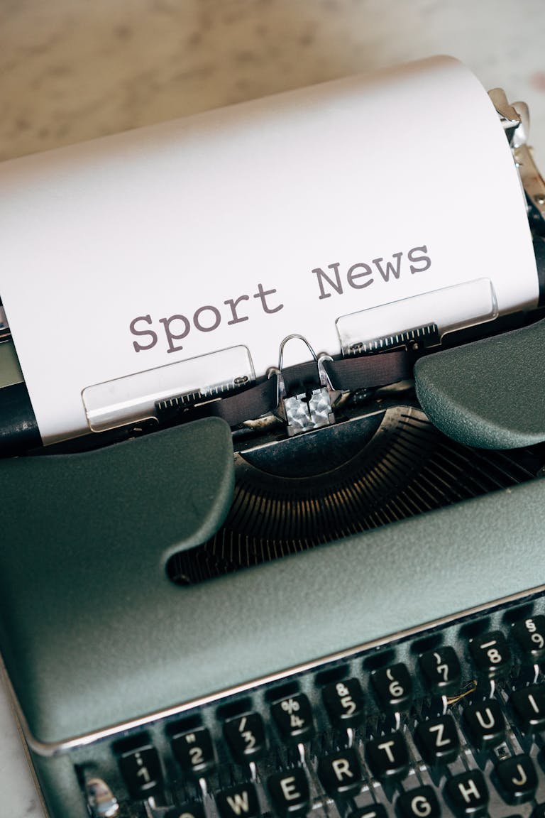 Close-up of a vintage typewriter printing 'Sport News' on paper, evoking retro writing themes.