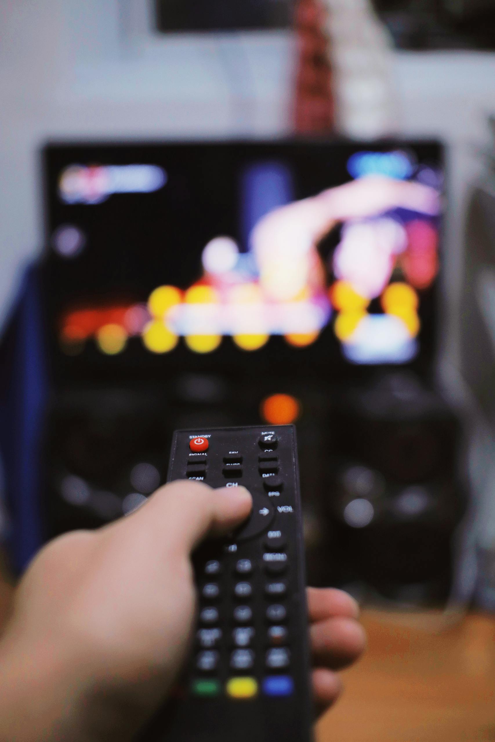 Crop unrecognizable person switching channels on remote control while watching TV on blurred background in light room during free time