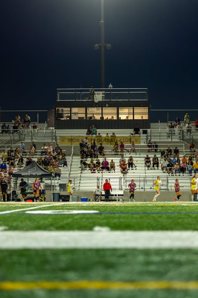 Football stadium under lights at night with spectators in the stands.