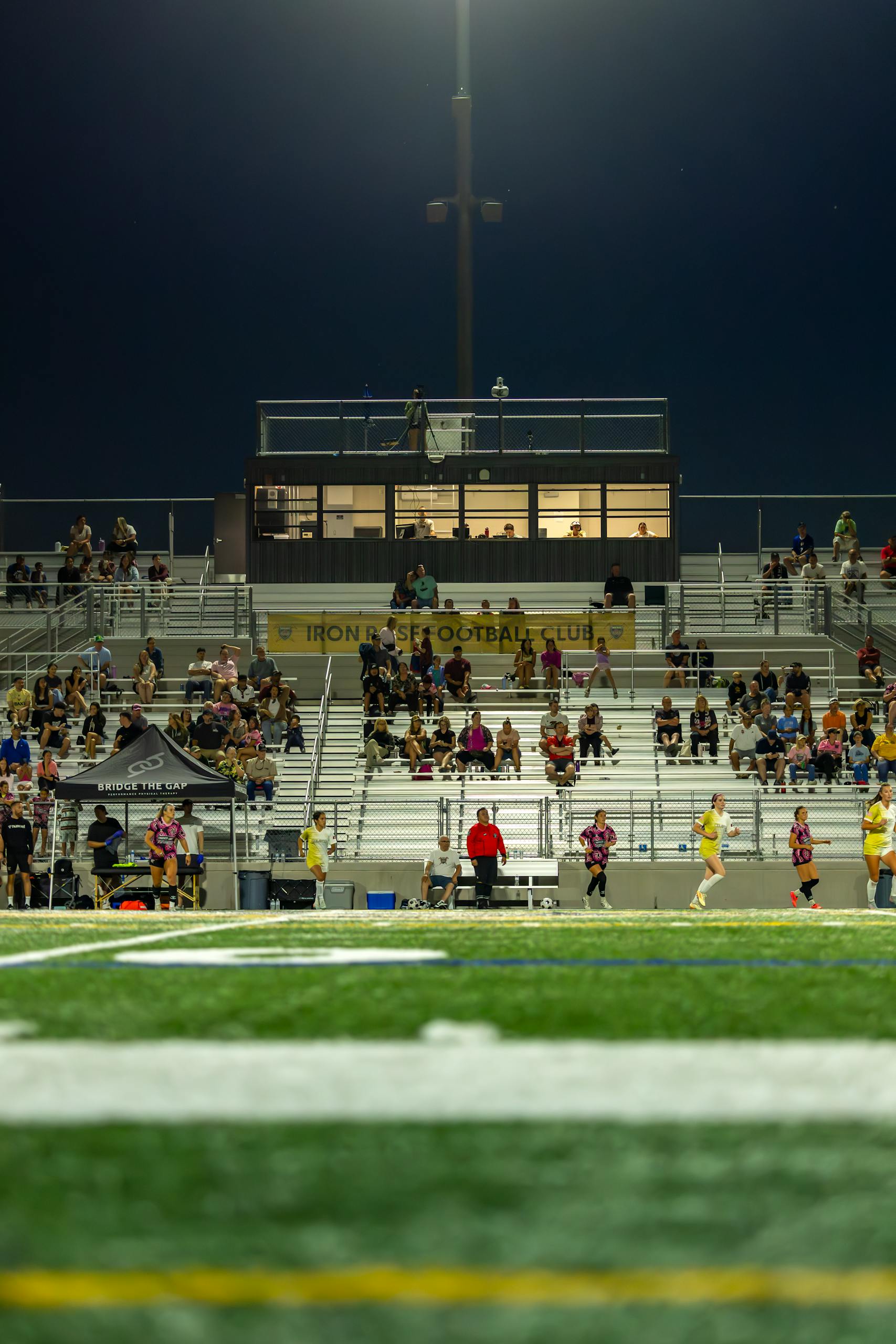 Football stadium under lights at night with spectators in the stands.