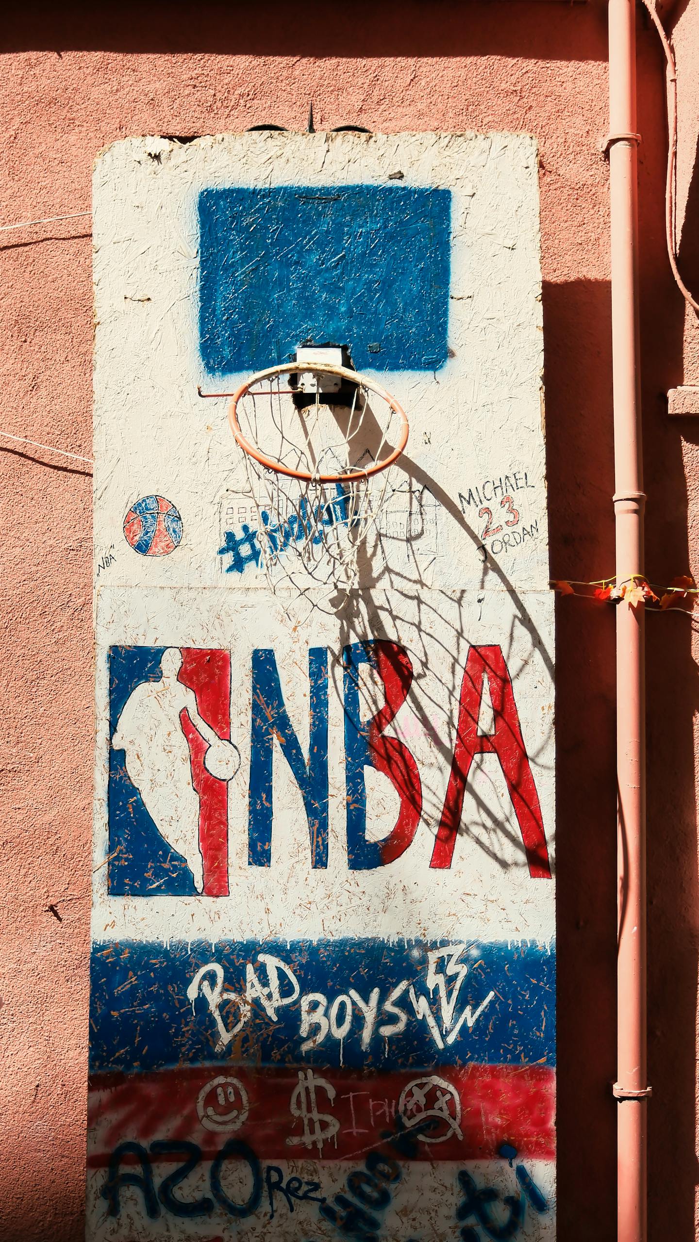 Graffiti-covered wall with a street basketball hoop, showcasing urban art style.