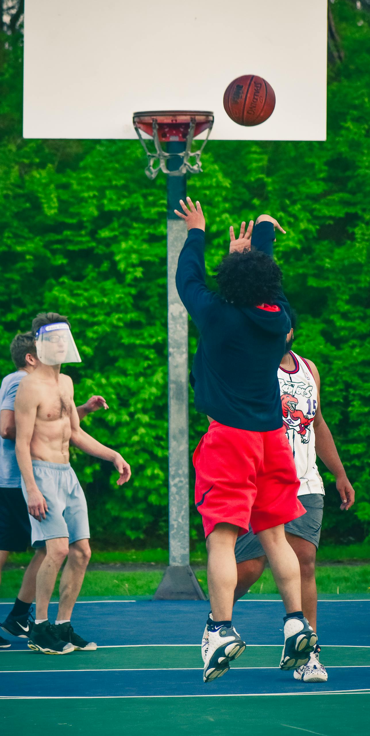Men playing basketball outdoors with face shield during pandemic.