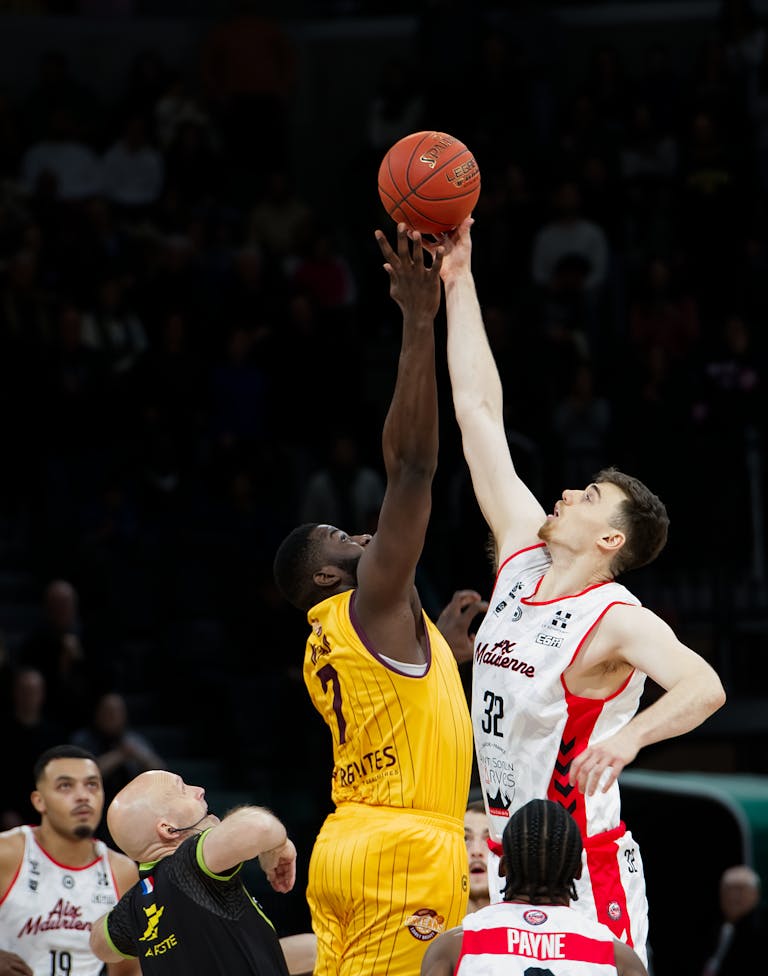 Two basketball players jump for the ball at the start of a thrilling game.