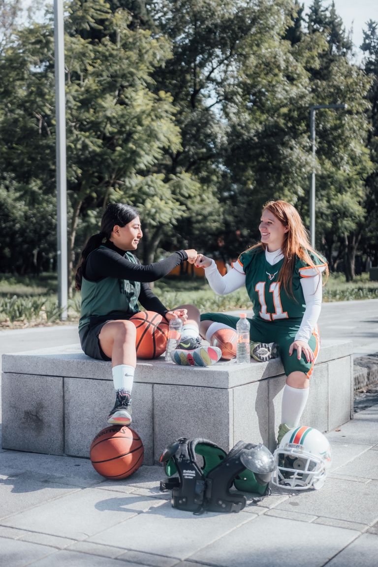 Two women in sportswear fist bump while sitting outdoors in Ciudad de México.
