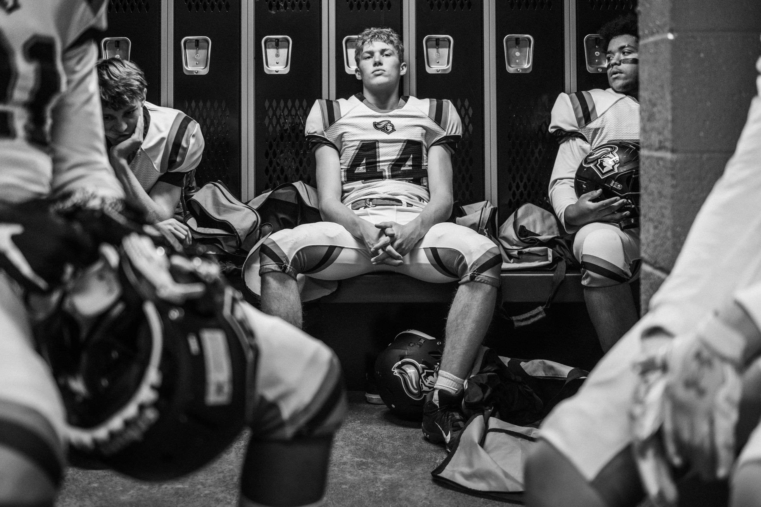 A black and white photograph of high school football players in a locker room pre-game.