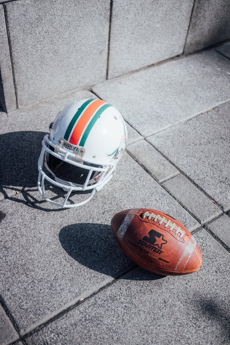 A close-up shot of an American football and helmet on a city sidewalk under sunlight.