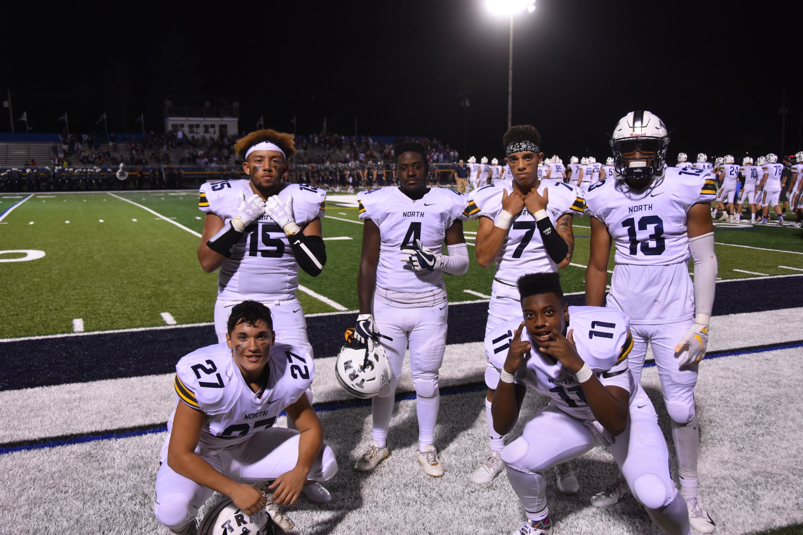 A group of high school football players posing on the field at night, wearing uniforms.