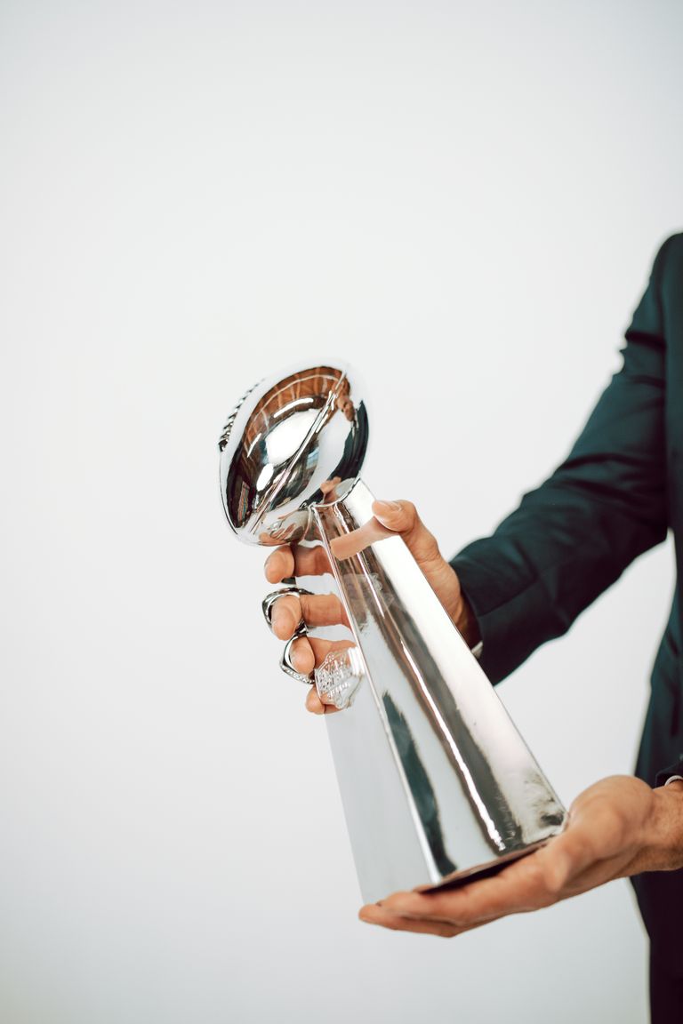 A person in a suit holding a sleek silver trophy against a white background.