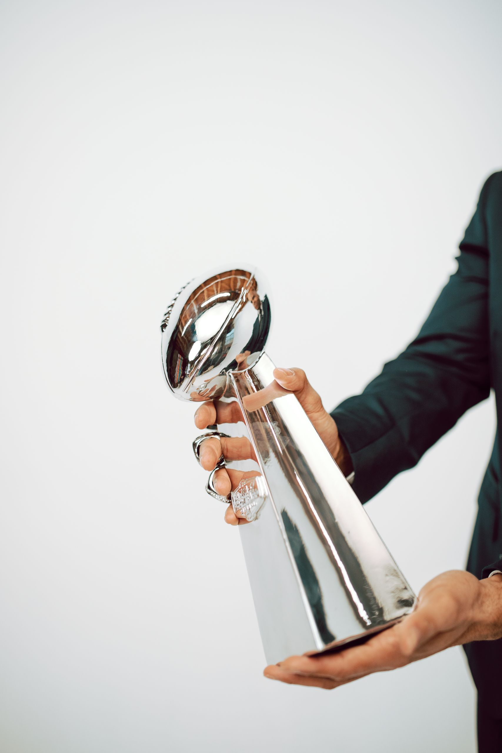 A person in a suit holding a sleek silver trophy against a white background.