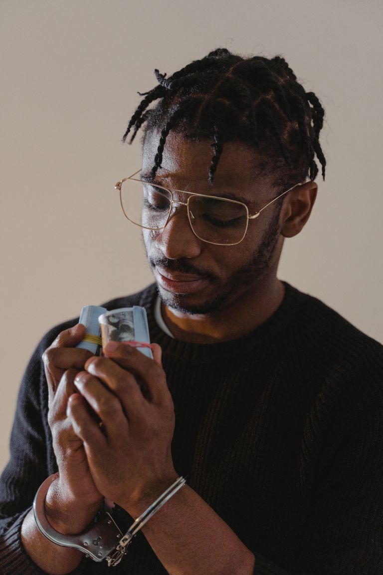 Adult man in handcuffs holding cash, reflecting a concept of crime and consequences.
