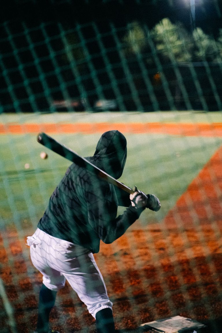 An athlete in a hoodie prepares to bat during a nighttime baseball game.