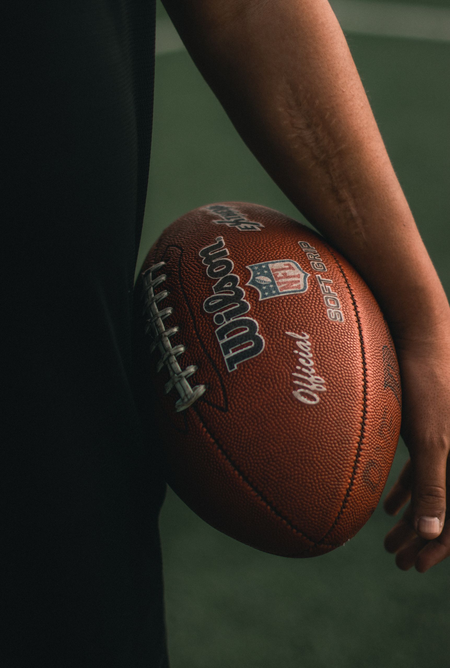 Detailed shot of a person's arm holding an official NFL football on a field.