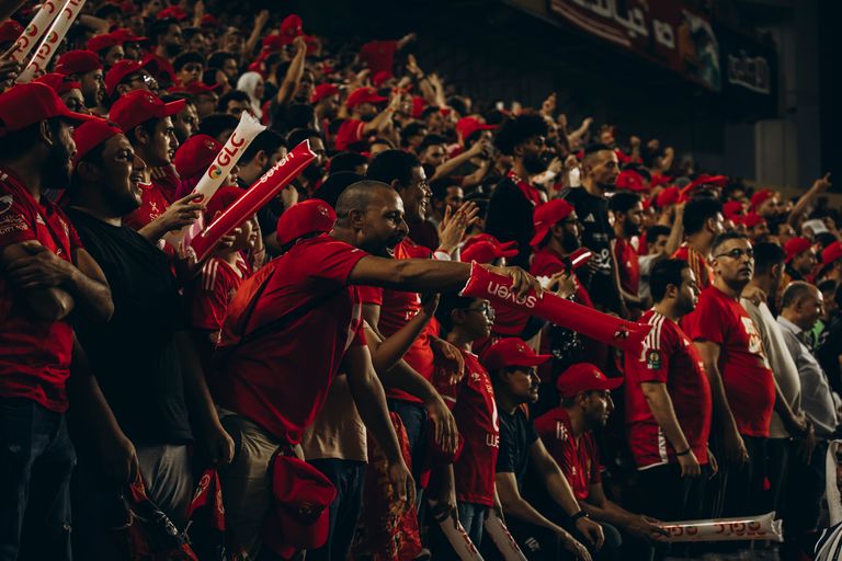 Excited football fans in red jerseys cheering passionately during a live match.