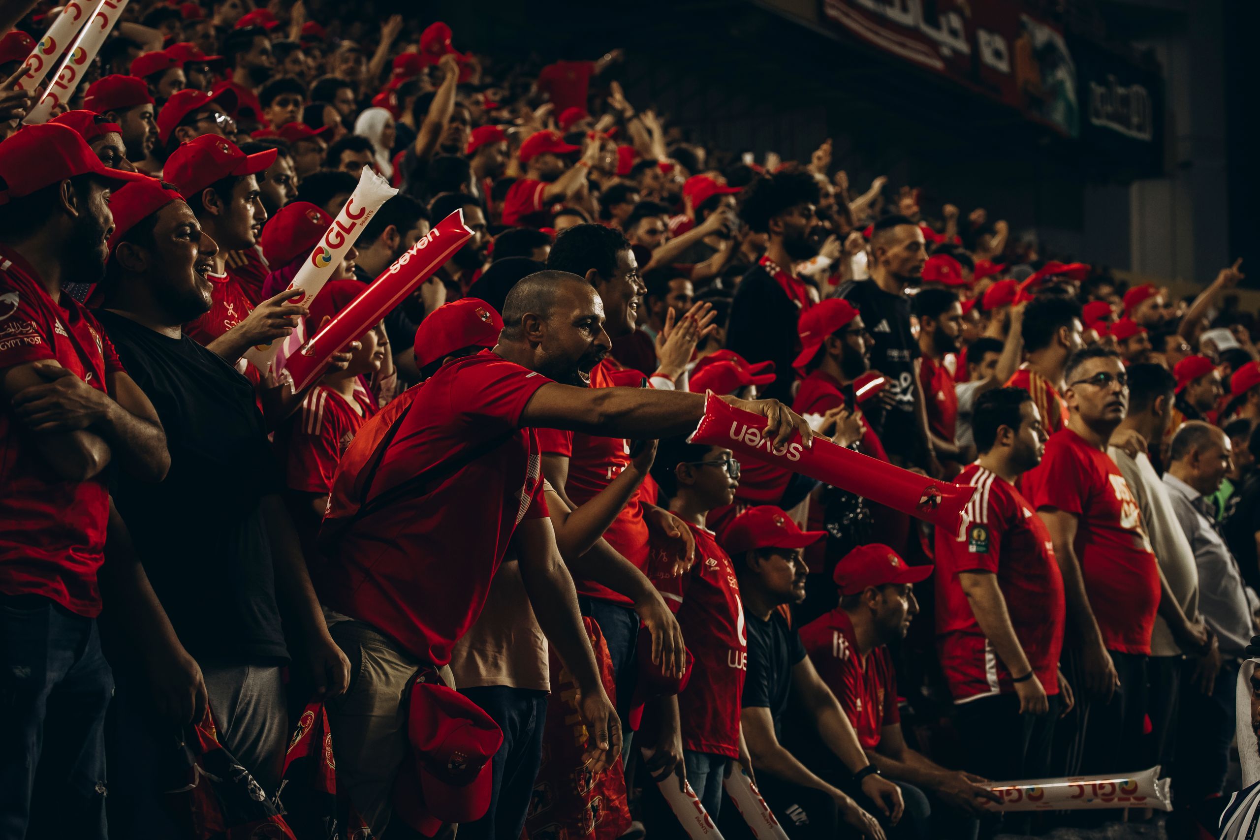 Excited football fans in red jerseys cheering passionately during a live match.