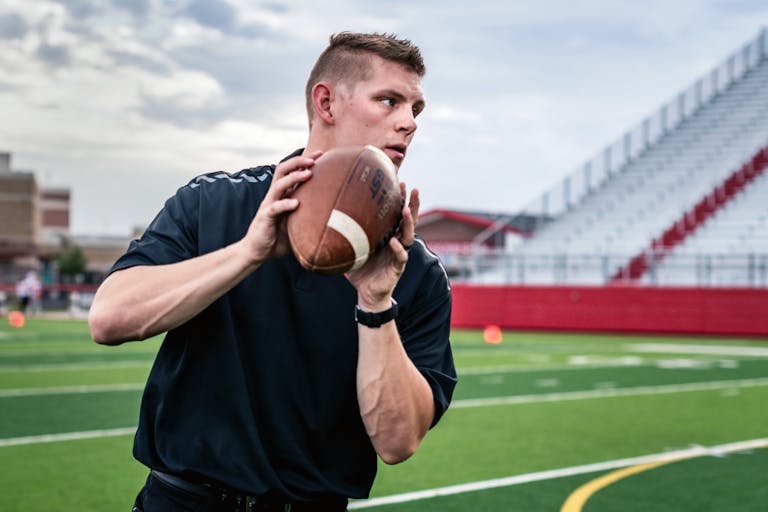Focused young man practicing throwing a football on a sunny day at a stadium.