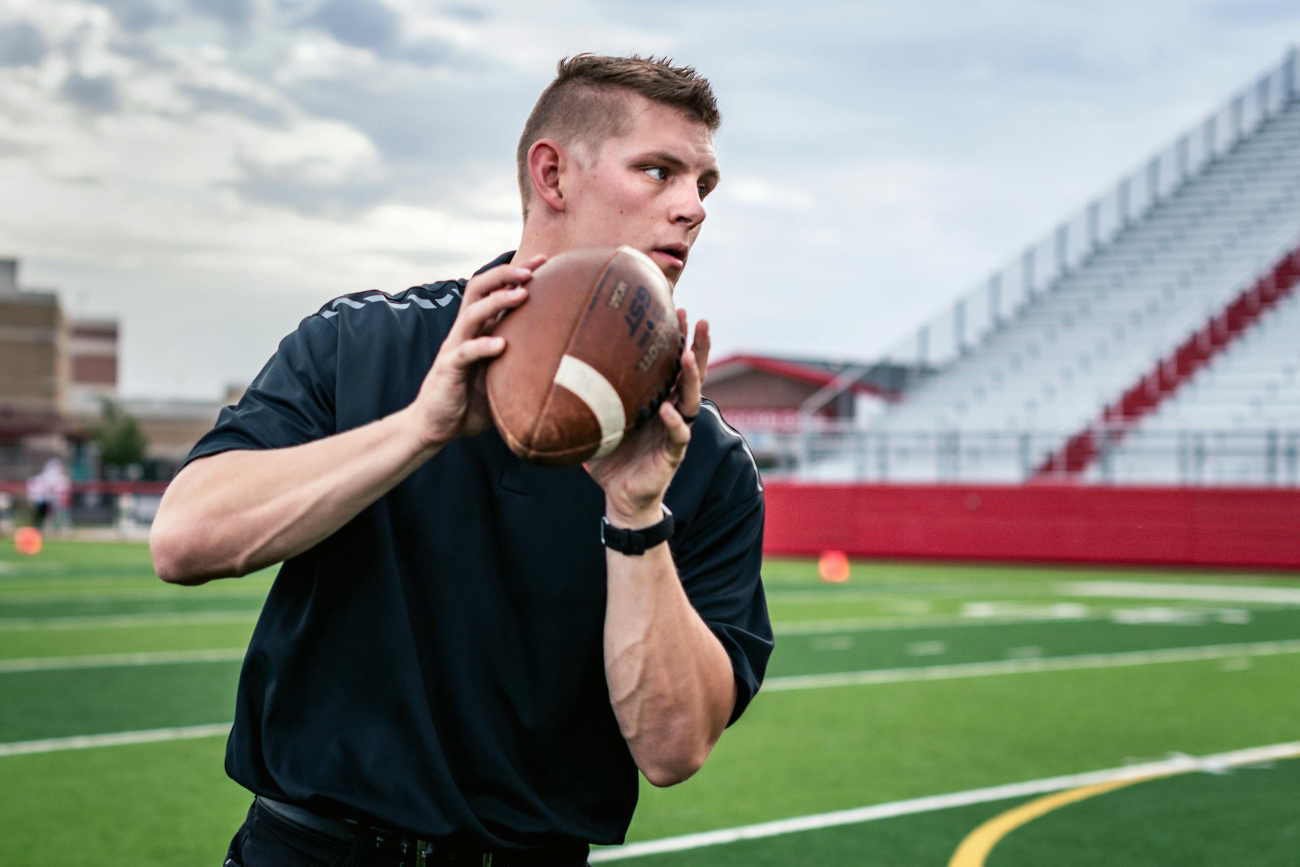 Focused young man practicing throwing a football on a sunny day at a stadium.