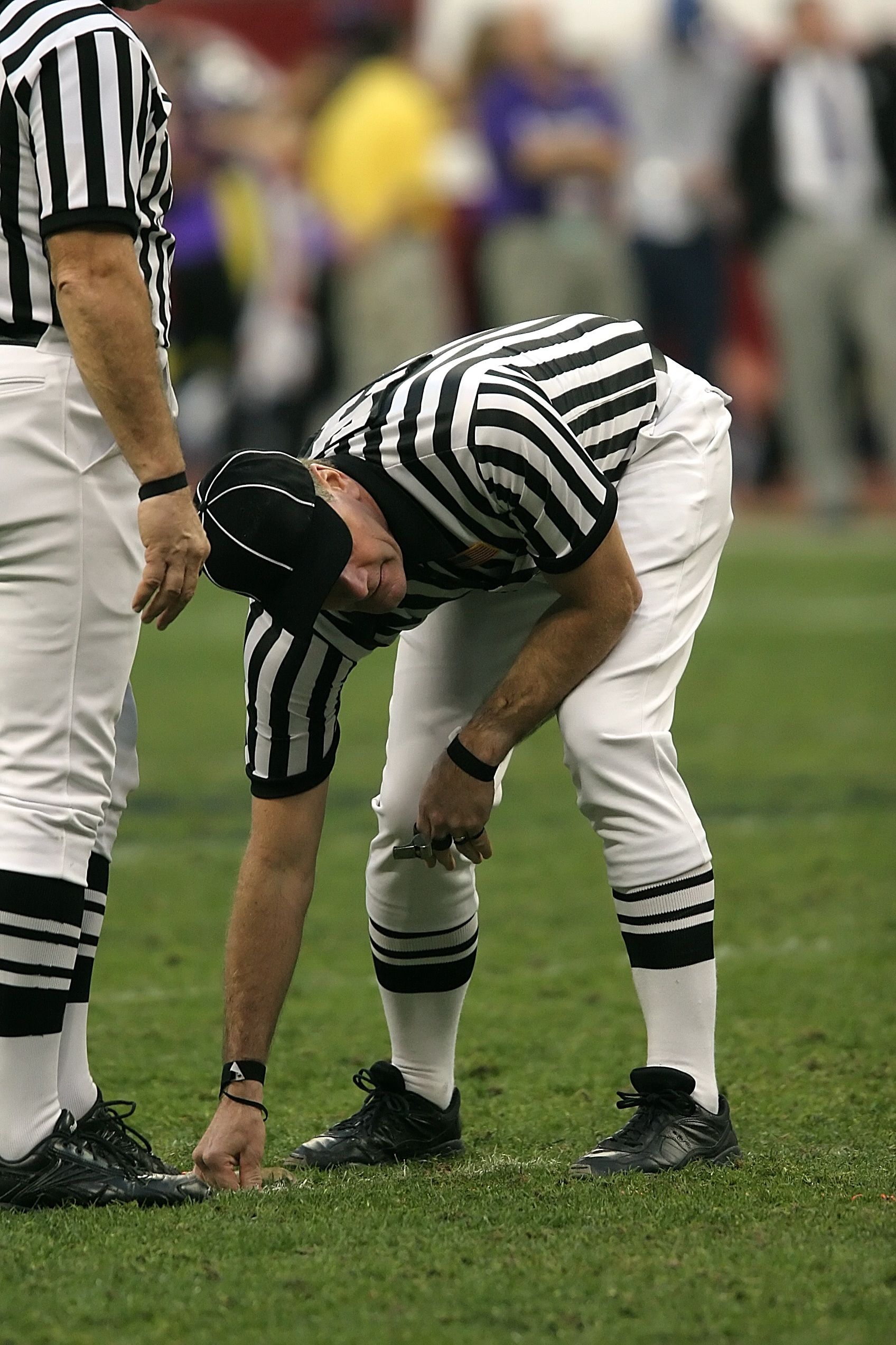 Football referee bends down to measure the yard line on a grass field during a game.