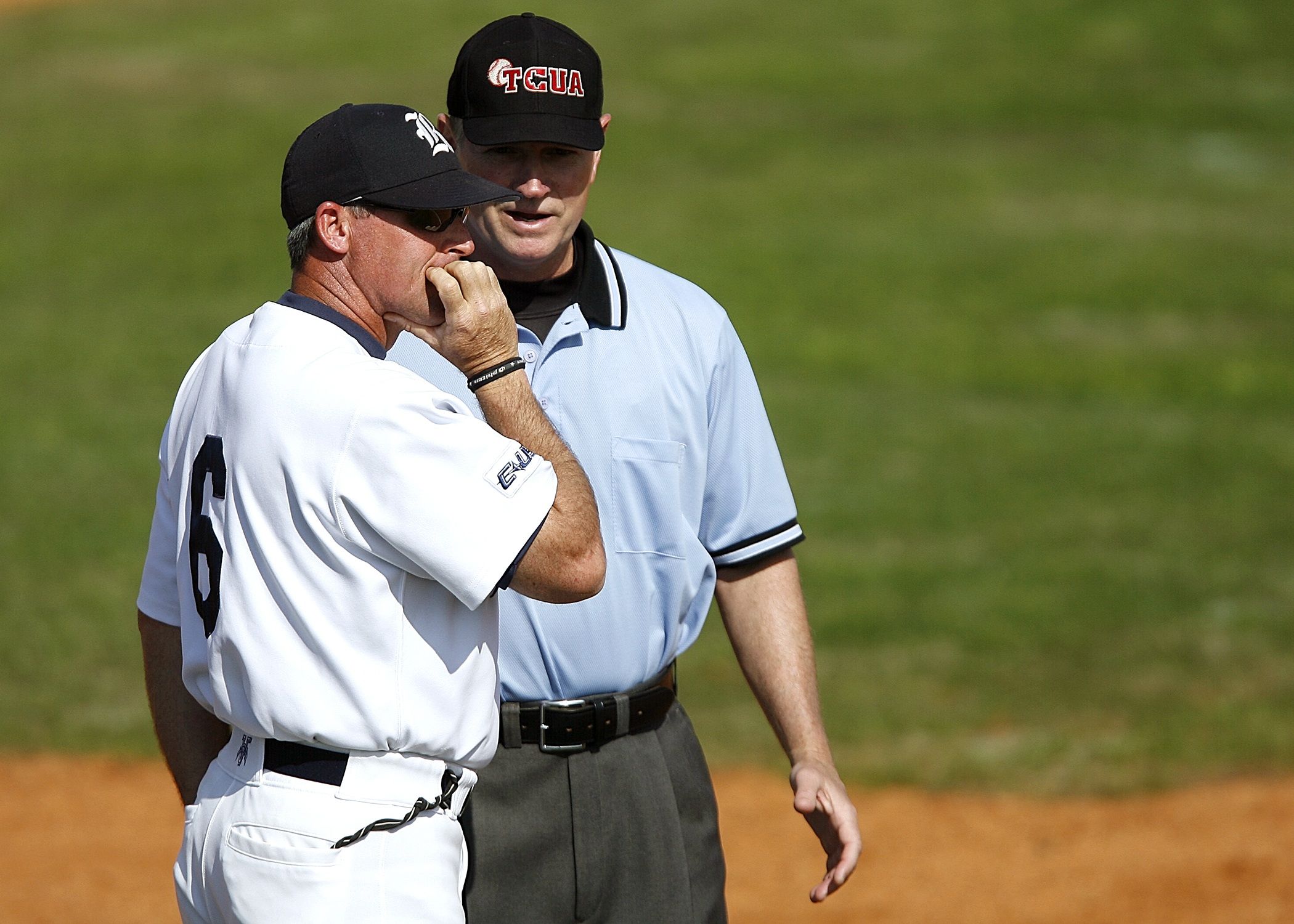 A baseball coach engages with an umpire on the field, discussing game strategy in uniform under a clear sky.