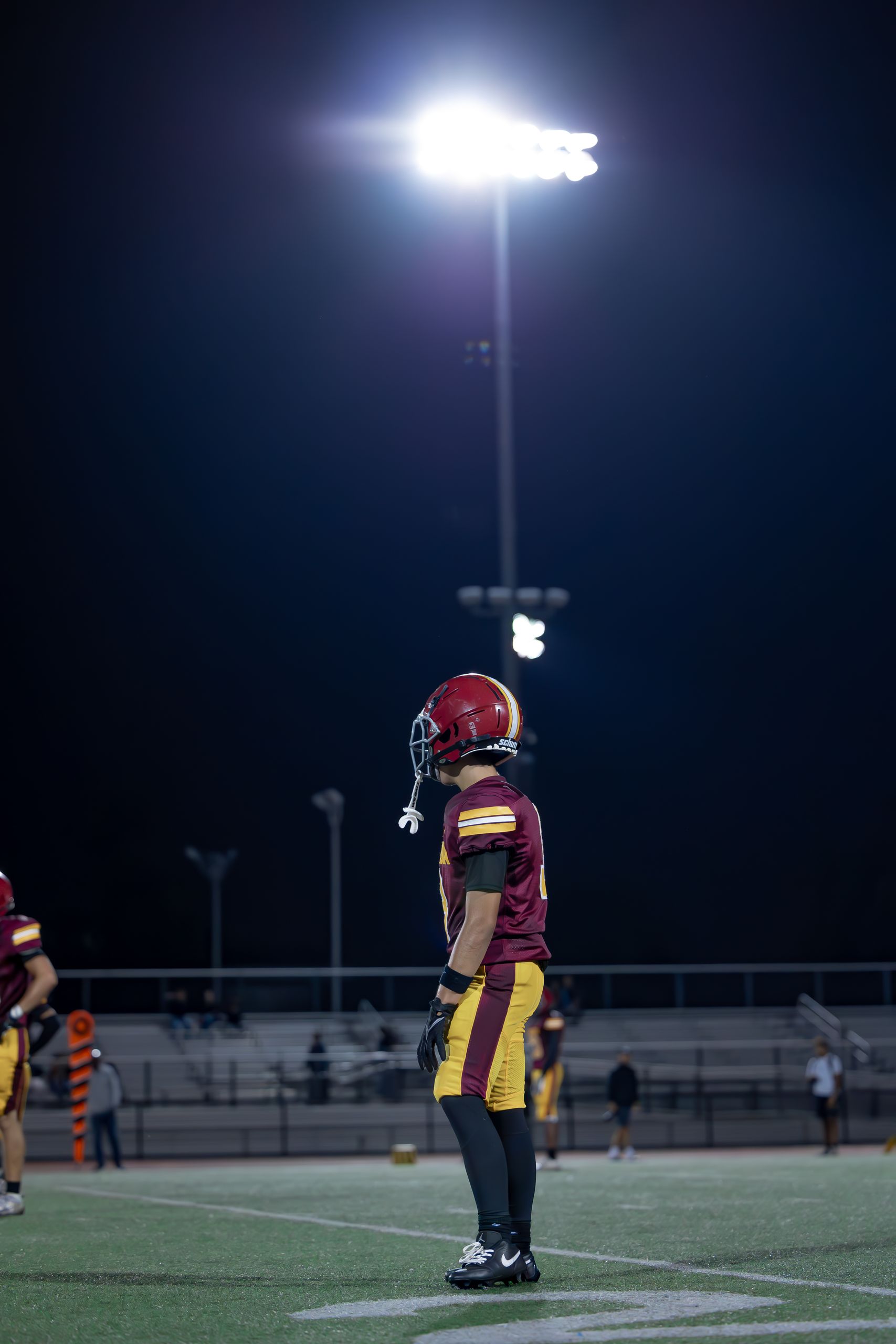 A football player stands under stadium lights at night, ready for action on the field.