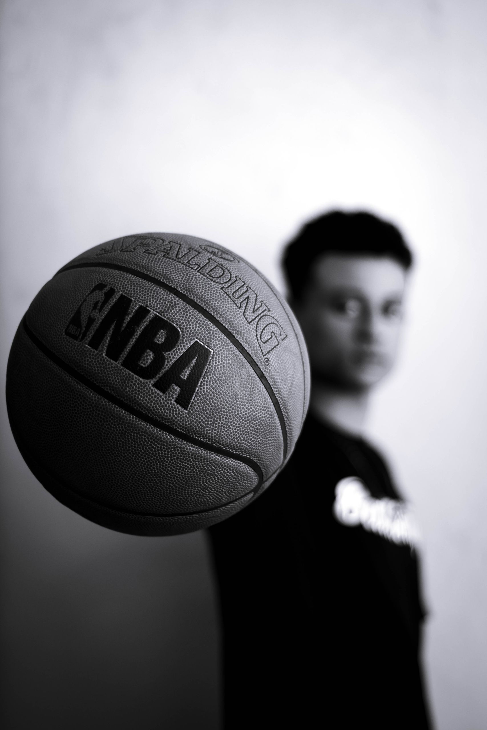 A stylish monochrome portrait of a man holding a basketball in focus, indoor studio setting.