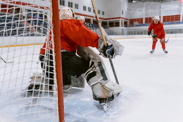 Action-packed ice hockey scene with goalie guarding the net on an indoor rink.