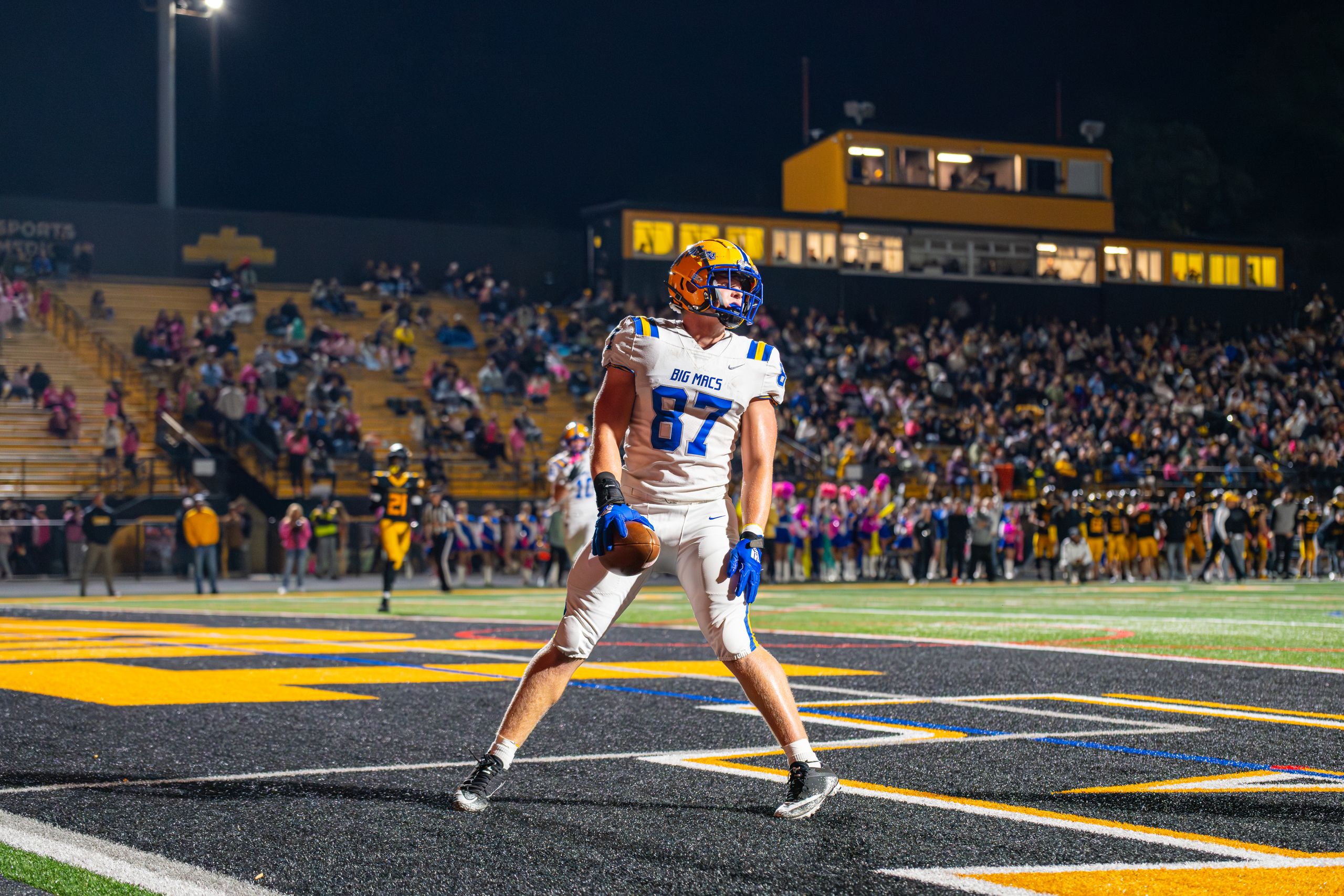 An excited football player celebrates a touchdown during a thrilling night game in a packed stadium.