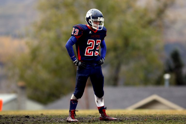 Athlete in full gear standing on football field, helmet and uniform visible.