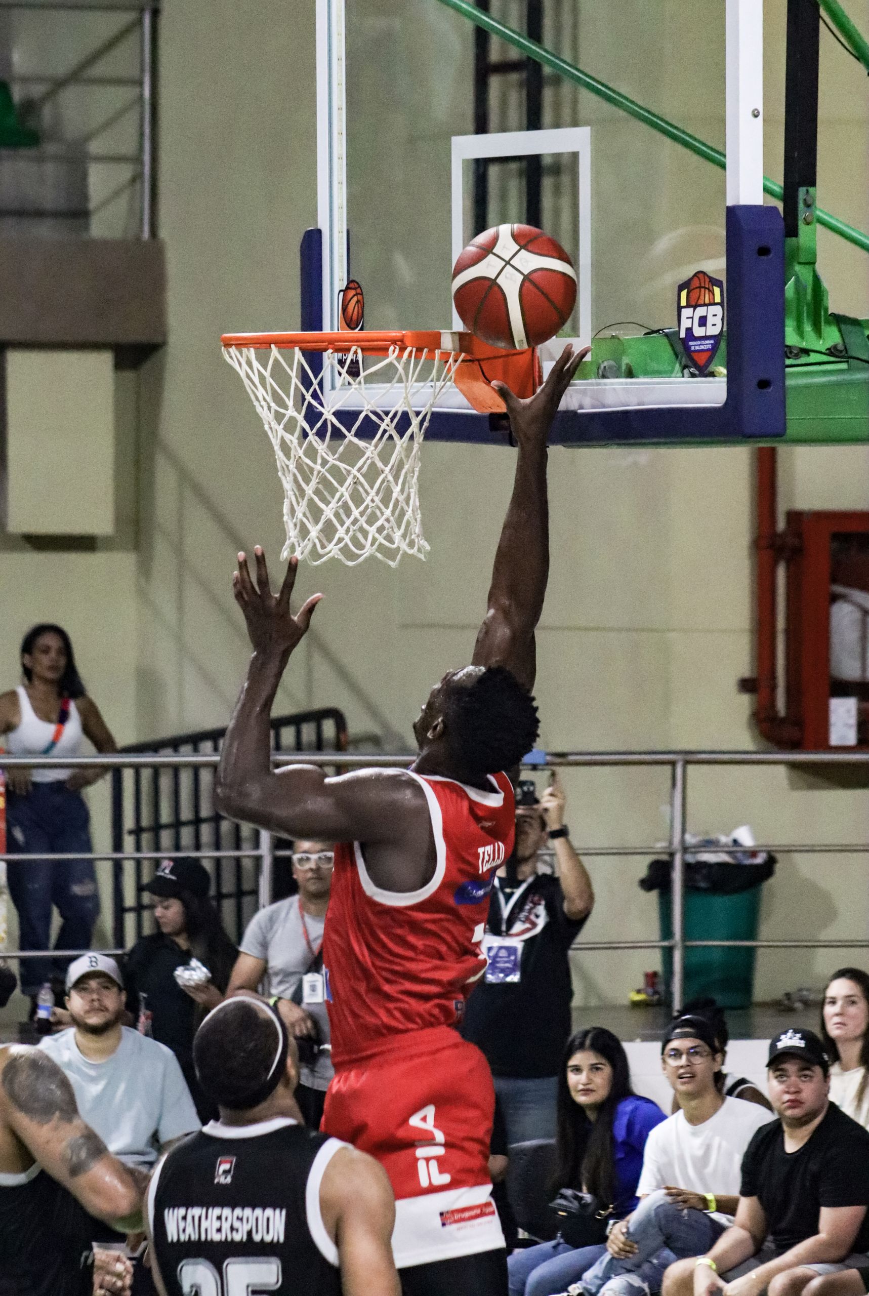 Basketball player making a dunk at an indoor game in Colombia. Energetic crowd in the background.