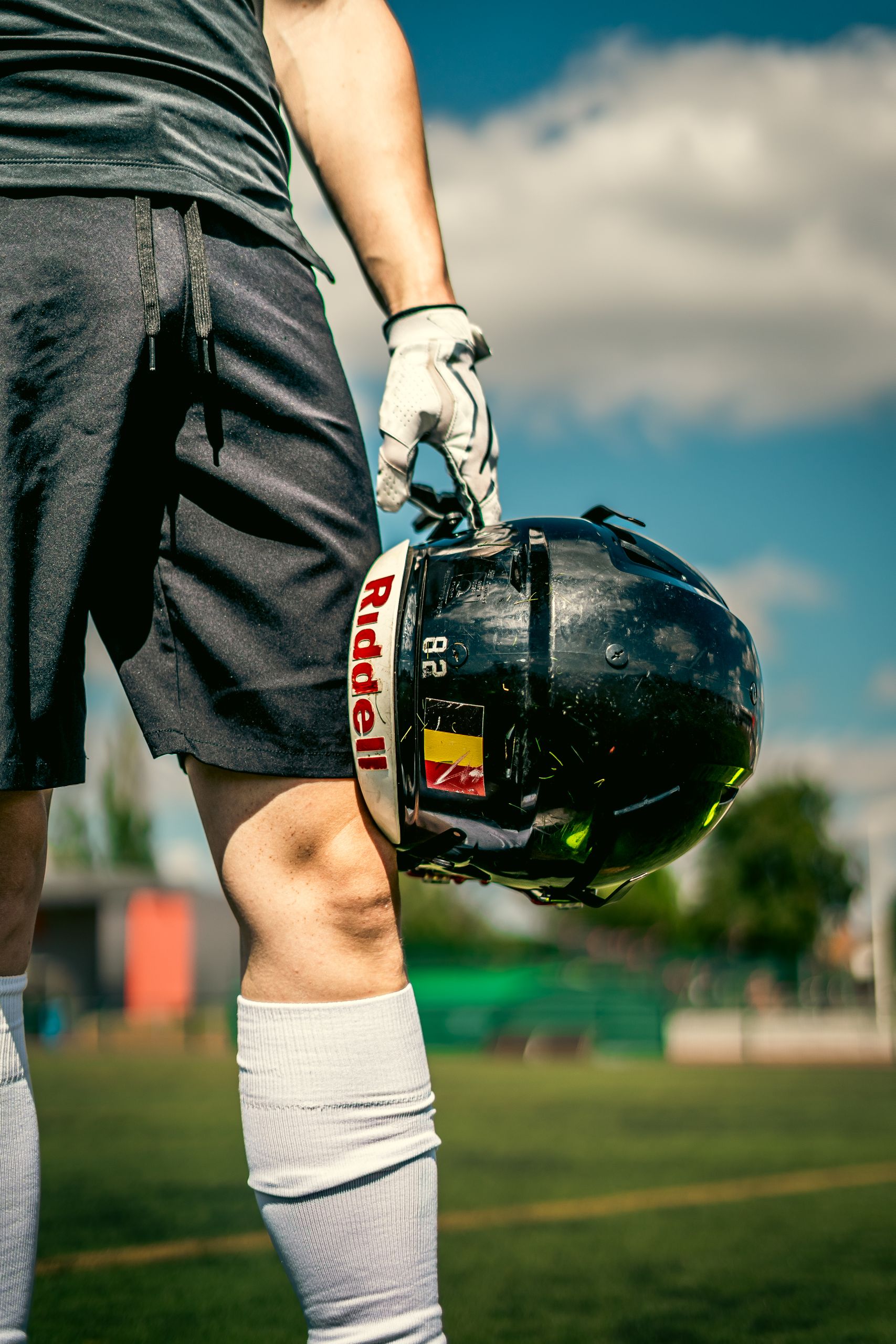 Close-up of an athlete holding a football helmet on a sunny day, showing sports attire and readiness.