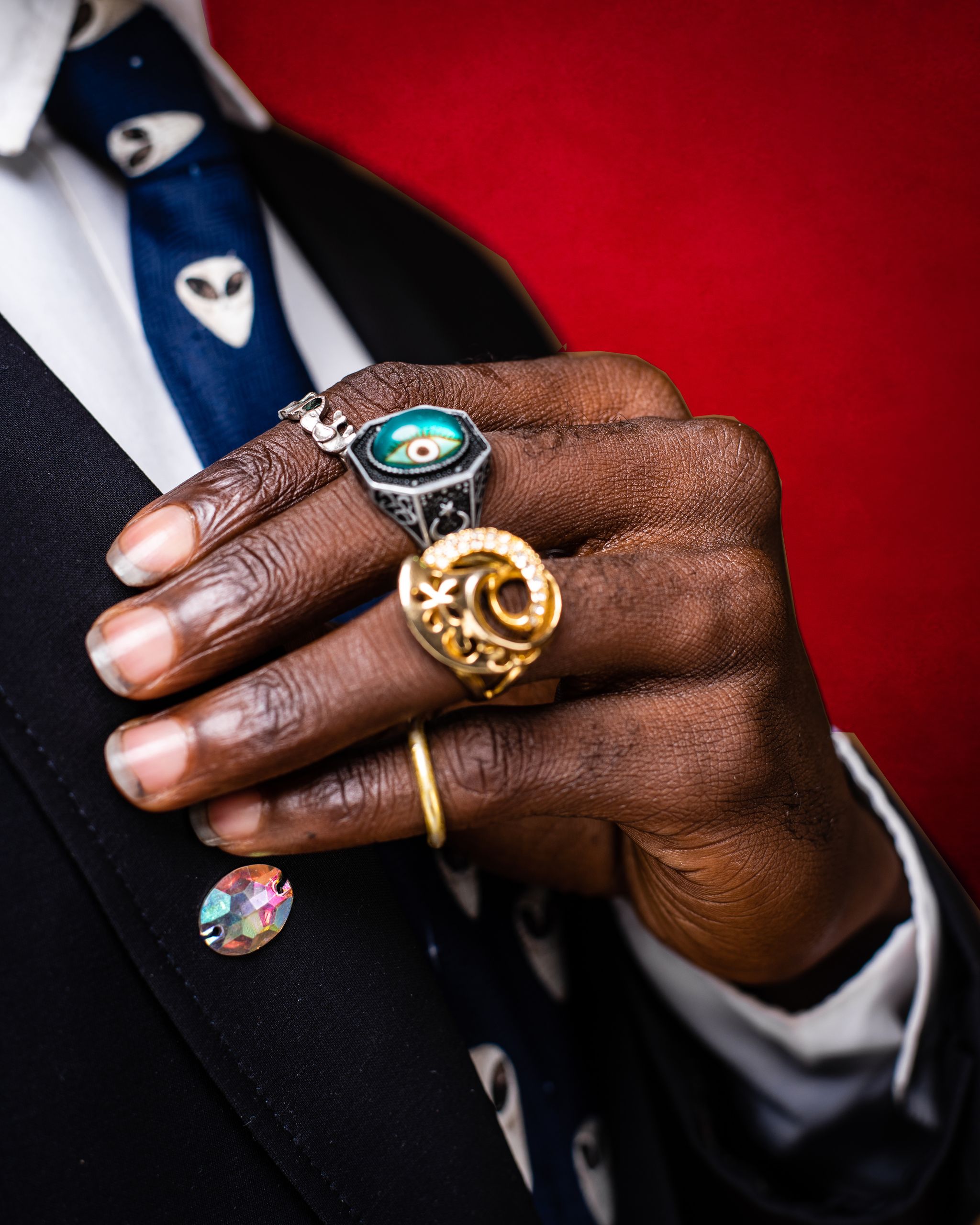 Close-up of hands with elegant rings beside a red textured background, showcasing style and fashion.