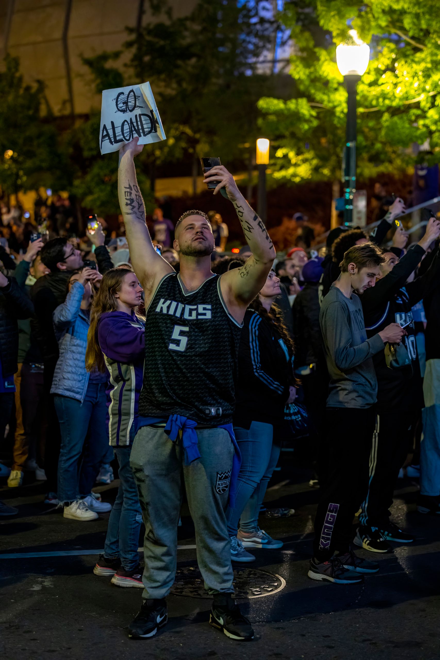 Crowd gathers to support basketball team during a vibrant evening street celebration.