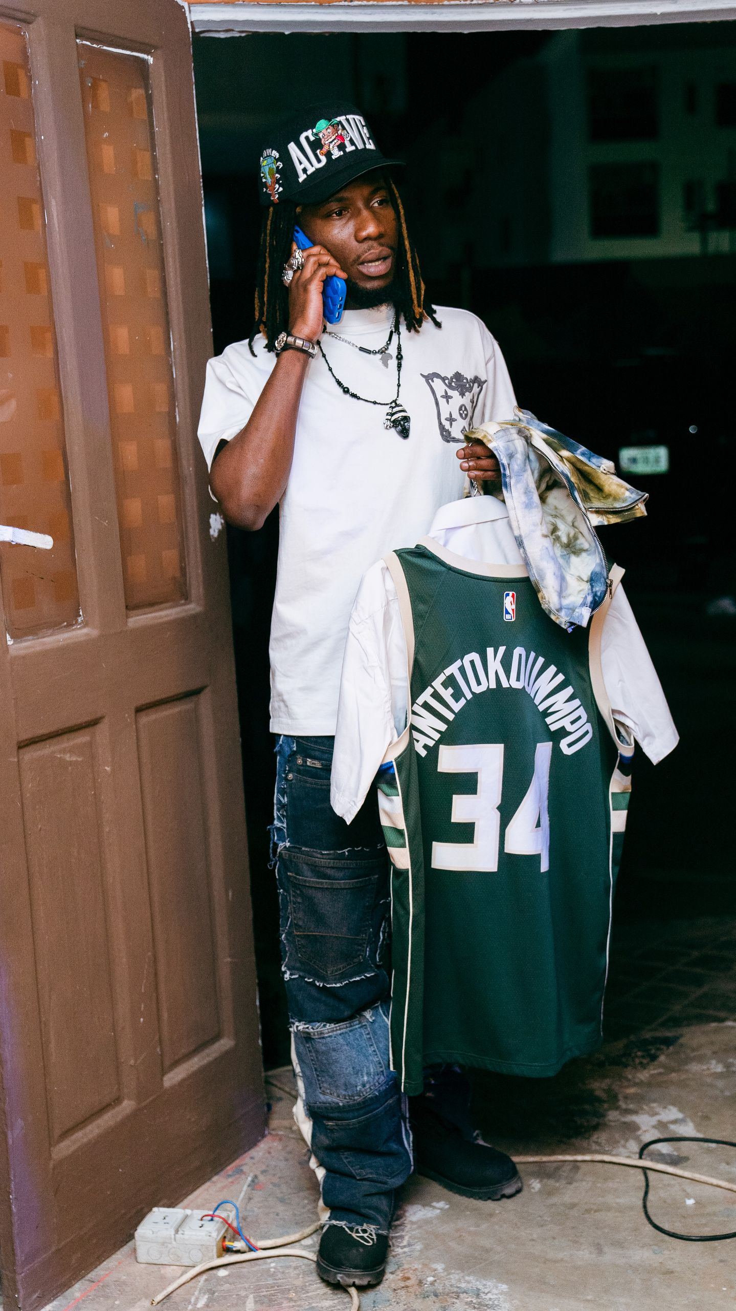 Man holds Antetokounmpo jersey in urban setting, wearing casual attire.